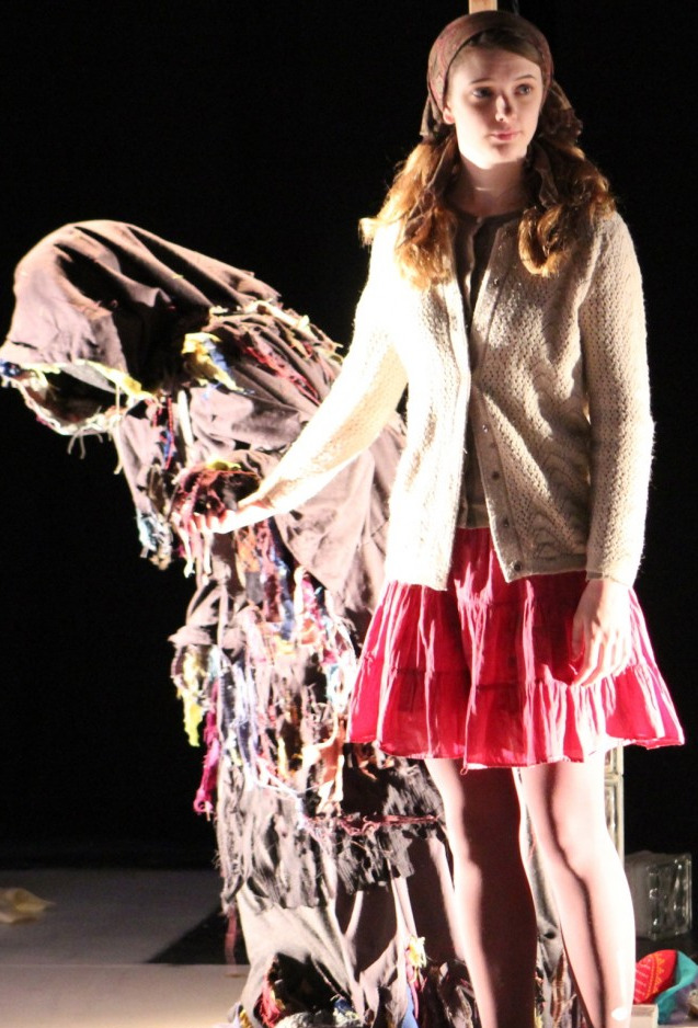 A girl holding the hand of a hunched figure in rags.